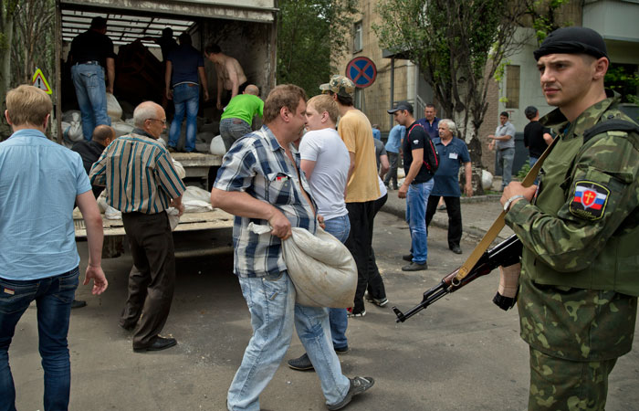 People carry sand bags to set up a shooting position as a pro-Russian gunman watches on the road leading from the the airport to Donetsk, Ukraine on Tuesday. President-elect Petro Poroshenko, known for his even-handed and pragmatic rhetoric, has vowed to negotiate a peaceful end to the revolts. (Vadim Ghirda/Associated Press)