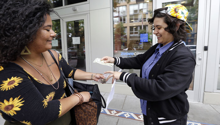 Yeni Sleidi, known as the "weed fairy," right, buys marijuana from a dealer, who declined to be identified, in Seattle’s Capitol Hill neighborhood Wednesday, May 28, 2014, where this past weekend Sleidi posted 50 fliers with nuggets of marijuana taped to them. Sleidi, a 23-year-old who works in social media, has been visiting Seattle from New York where last year she did a similar posting, albeit anonymously. (AP Photo/Elaine Thompson)