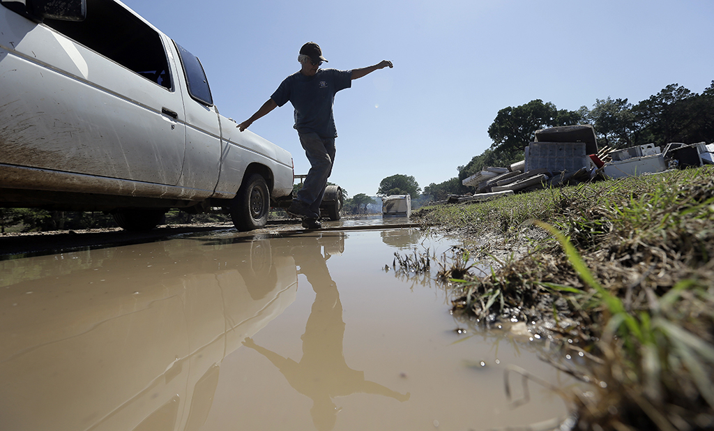Johnny Rodriguez uses a plank to cross standing water as he works along the Blanco River, Friday, May 29, 2015, in Wimberley, Texas. Search efforts continue for those persons who went missing from the Memorial Day weekend floods in Central Texas. (AP Photo/Eric Gay)