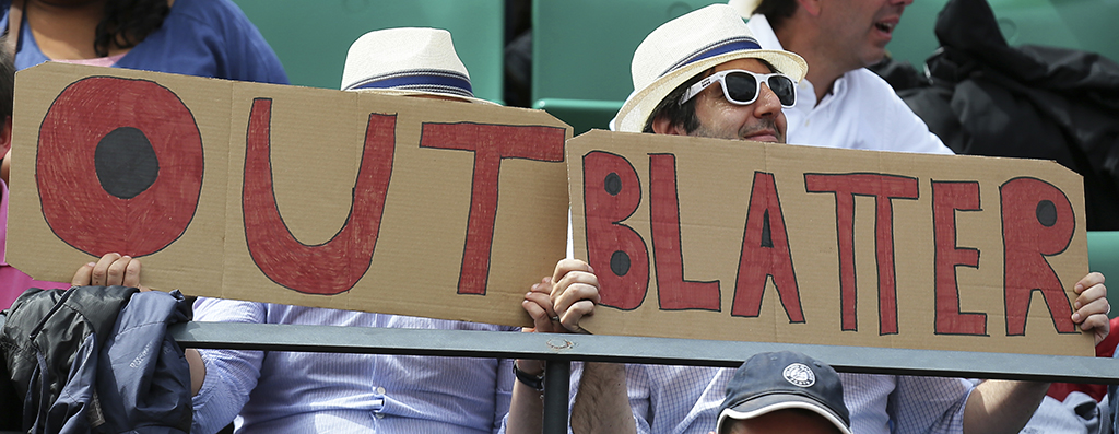 Two spectators hold signs reading "Out Blatter", referring to newly re-elected FIFA president Sepp Blatter during the quarterfinal match of the French Open tennis tournament between Spain's Garbine Muguruza and Lucie Safarova of the Czech Republic at the Roland Garros stadium, in Paris, France, Tuesday, June 2, 2015. Blatter said Tuesday he will resign from his position amid corruption scandal. (AP Photo/David Vincent)